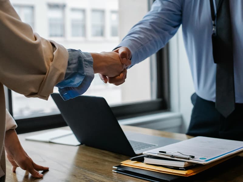 handshake between a man and woman over a laptop