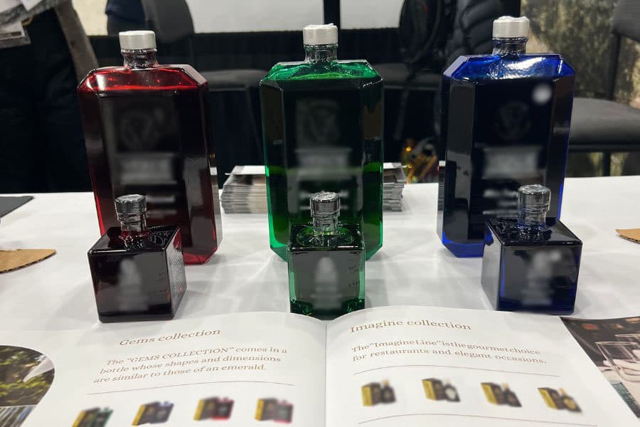 Three olive oils in red, blue, and green glass emerald shaped bottles that look like a personal care item or spirit
