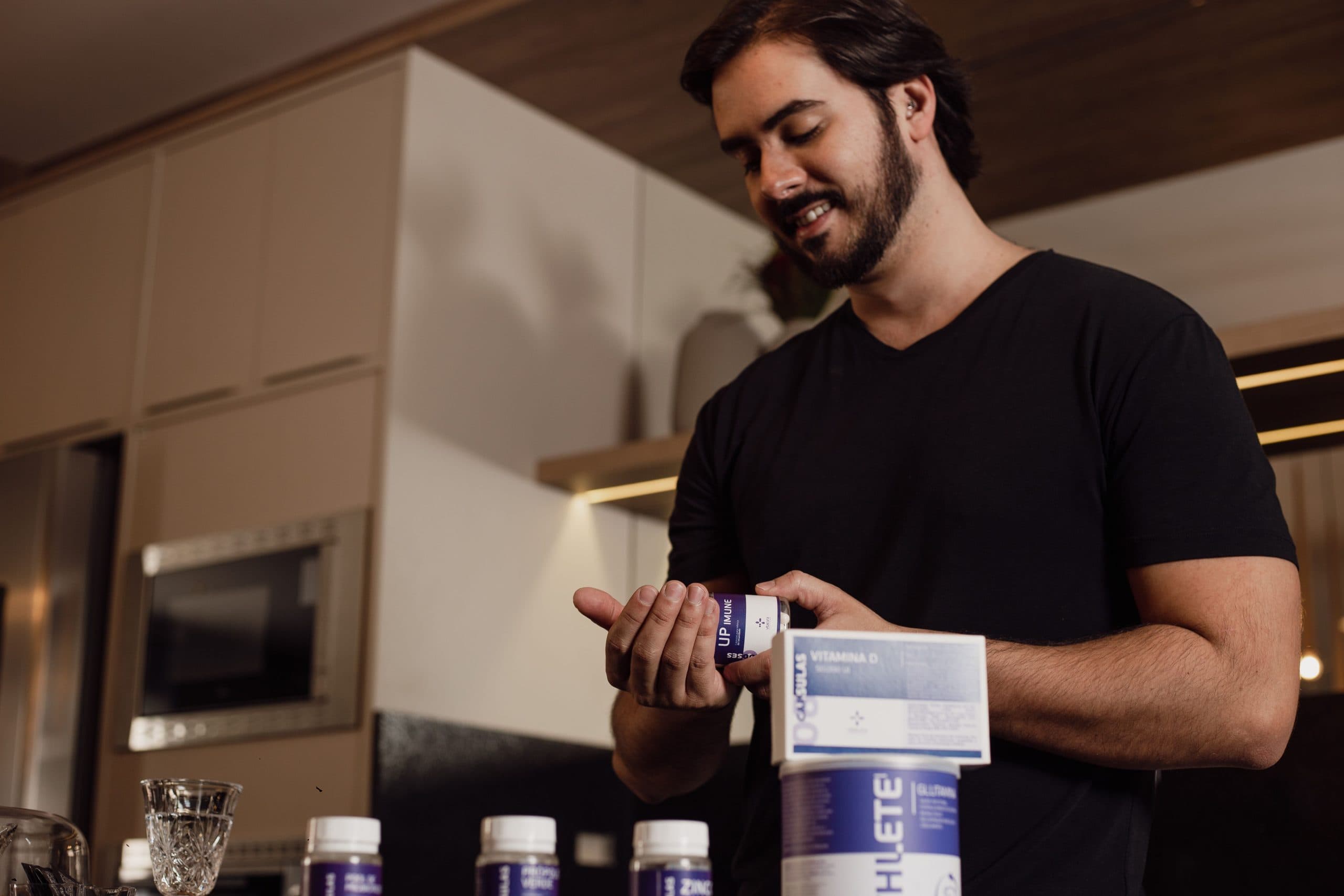 Man in black shirt standing in a kitchen and looking at supplement bottle