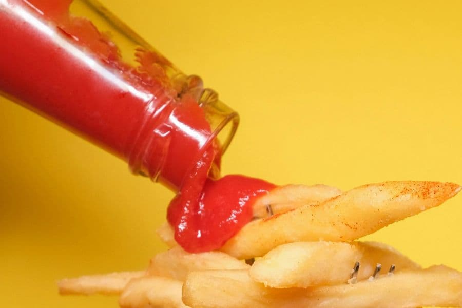 glass condiment bottle pouring ketchup onto fries