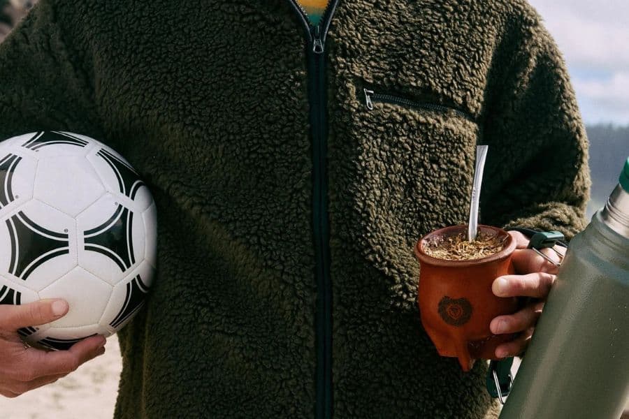 Person holding a soccer ball in one hand and a traditional yerba mate gourd in the other.
