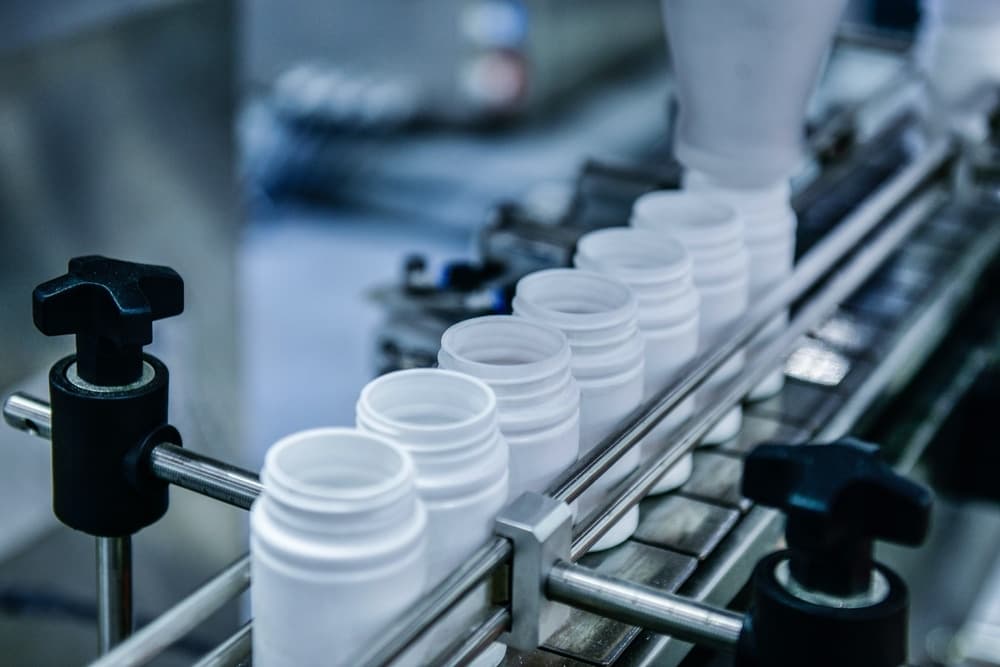 white plastic pharmaceutical packaging bottles on conveyer belt