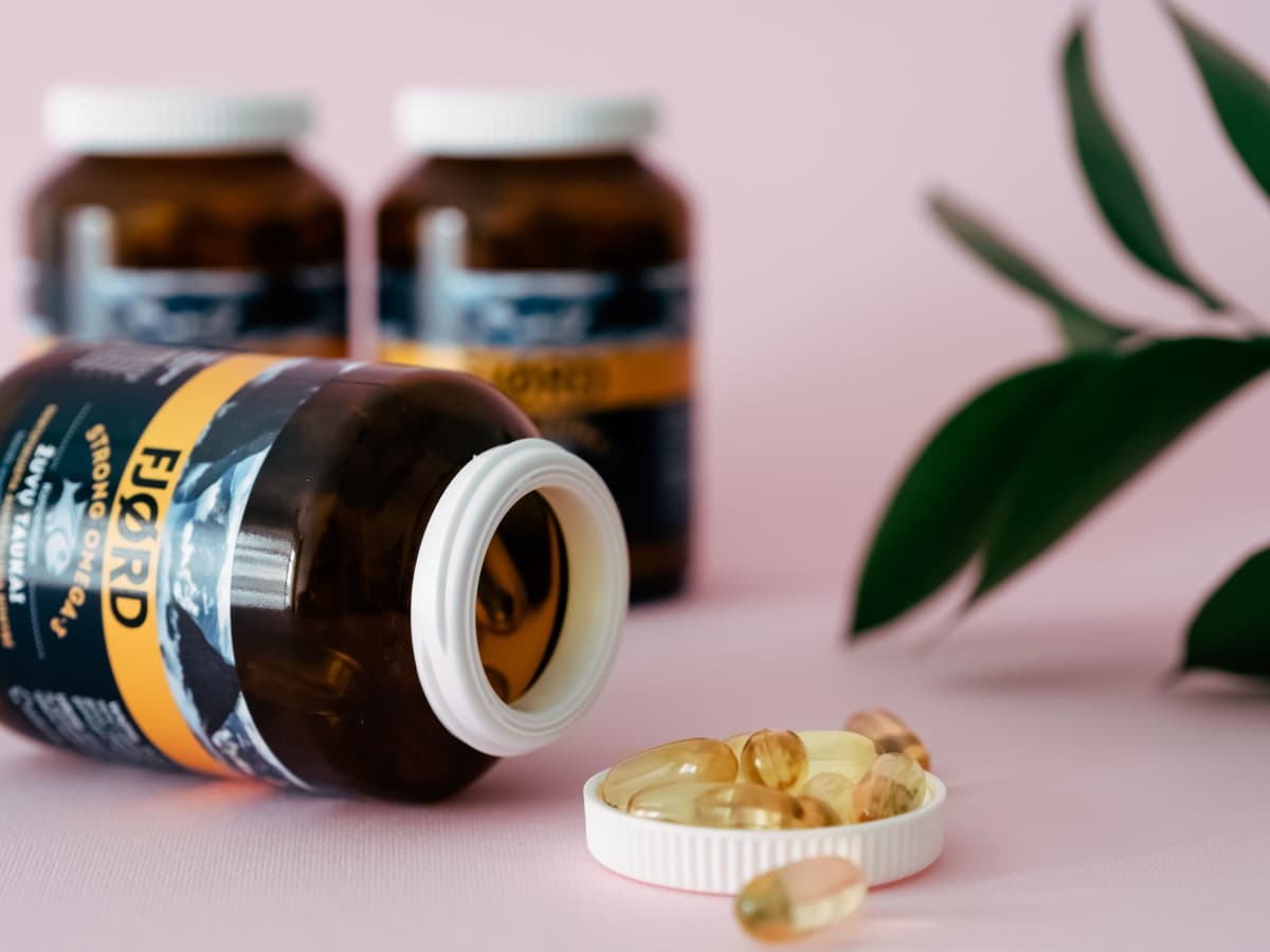 pill bottle laying on side with 2 bottles in the background. Transparent yellow capsules spill out of bottle in lid and surrounding.